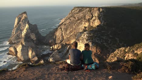 couple of backpack tourists sitting at cliff