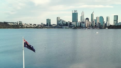 aerial, drone in shot flying close to australian flag, river and city skyline in background