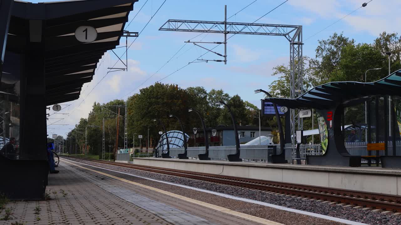 Timelapse or time lapse footage of people at a train station waiting for orange trains. Boarding them and getting off and waiting in the middle of it. Summer time with blue skies and trees in the back