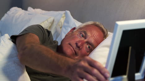 sad senior man lying in bed looking at photo frame