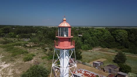 Beautiful-aerial-view-of-white-painted-steel-lighthouse-with-red-top-located-in-Pape,-Latvia-at-Baltic-sea-coastline-in-sunny-summer-day,-wide-angle-drone-shot-orbit-right