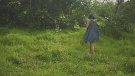 rack focus of woman in blue dress walking up grassy hill, stops to look around