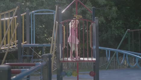 plano general de una niña de 4 años en rosa jugando en una estructura en un patio de recreo