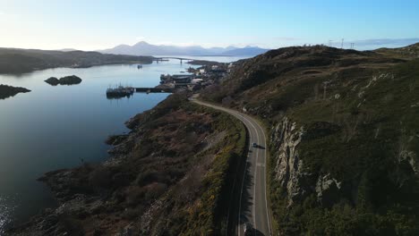 Fliegen-Entlang-Der-Straße-Nach-Kyle-Of-Lochalsh-Mit-Verkehr,-Ein-Schwenk-Nach-Oben-Zeigt-Die-Skye-Bridge-Und-Die-Cuillin-Mountains-Im-Schottischen-Hochland