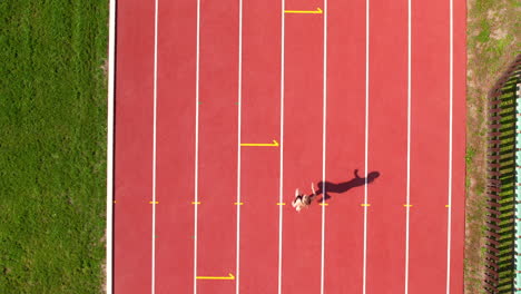 aerial shot of an athlete sprinting on a red track, casting a long shadow to the side under the midday sun