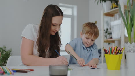 una familia de dos niños y una joven madre sentada en la mesa dibuja en papel con lápices de colores. desarrollo de la creatividad en los niños.