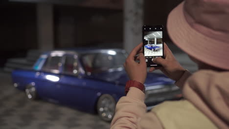 person taking photo of a classic blue car at night