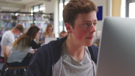 estudiante masculino trabajando en la computadora en la biblioteca de la universidad