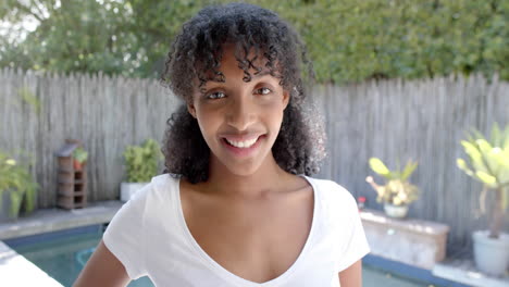 happy biracial woman with long curly hair in white t shirt, smiling in sunny garden, slow motion