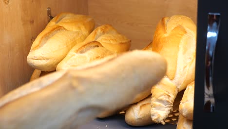 a person's hand reaching for a baguette in a bakery