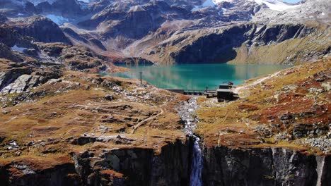 Vista-Aérea-De-La-Cascada-Que-Fluye-Hacia-El-Acantilado-De-La-Montaña-Desde-El-Aliviadero-Del-Embalse-De-Weisssee-En-Austria