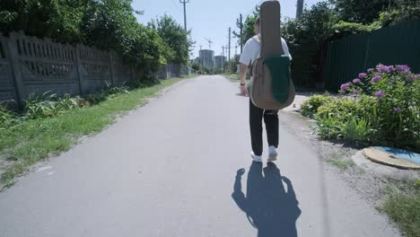 young man walking with guitar on street near forest