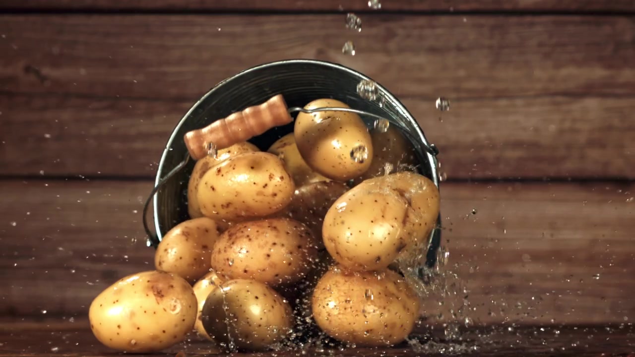 Patate fresche che cadono da un secchio con schizzi d'acqua al rallentatore