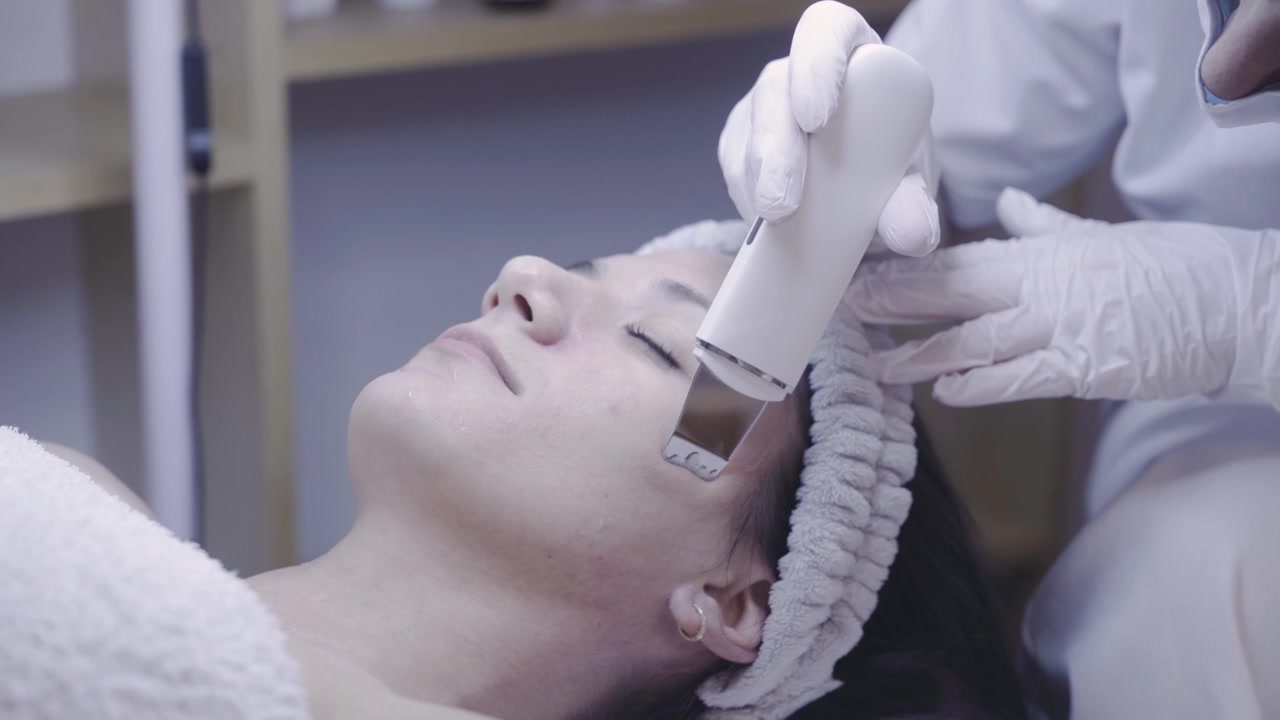 Scrubber cutaneo a ultrasuoni che scivola su un viso rilassato in una struttura tranquilla