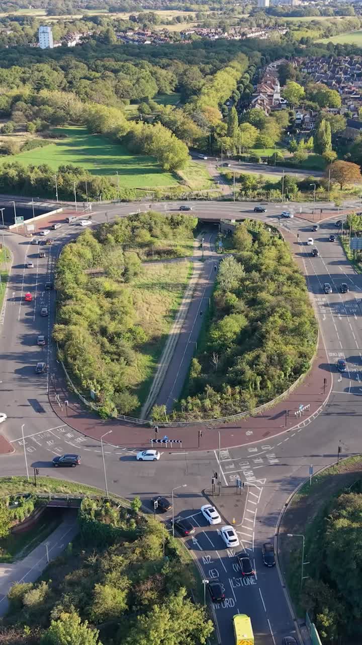 Vertical aerial drone descending over Green Man Roundabout, Leytonstone, London. The junction nearest the camera is halted at a red light, while the view expands to reveal sky and blue horizon above