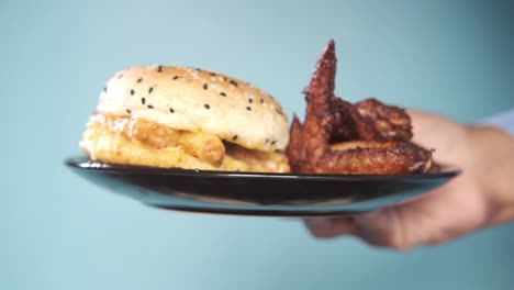 mano sosteniendo un plato con hamburguesa y alas de pollo