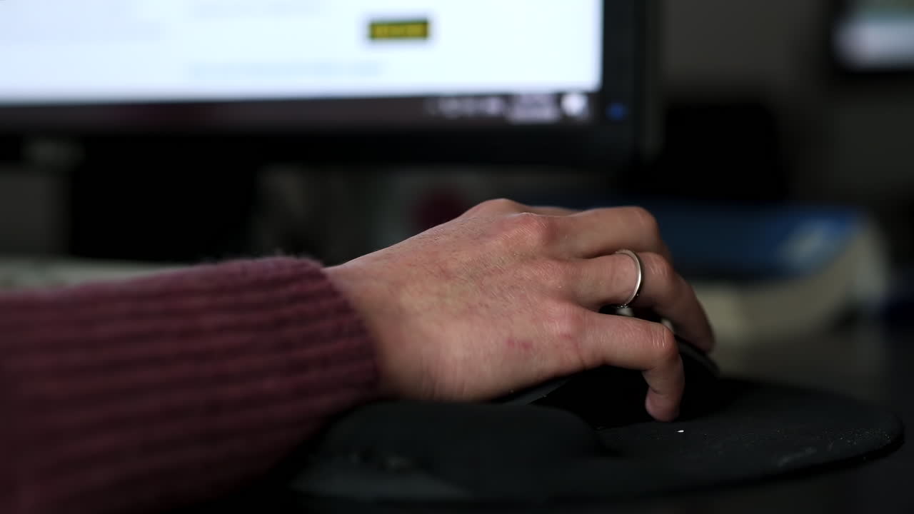 A hand navigates a computer mouse while working in an office environment. The scene highlights the activity of typing and managing digital tasks on a desk