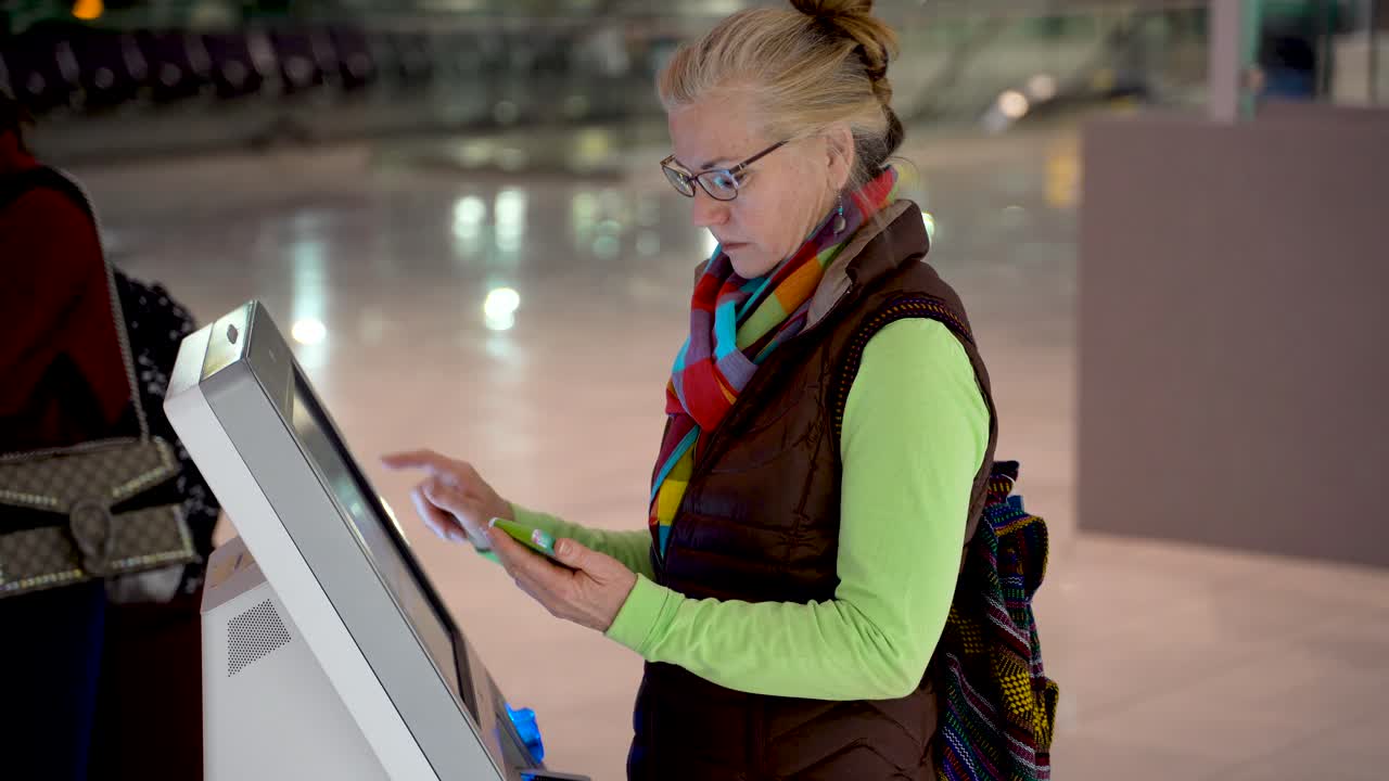 mujer bonita y madura sosteniendo un teléfono inteligente y haciendo un autochequeo en el aeropuerto