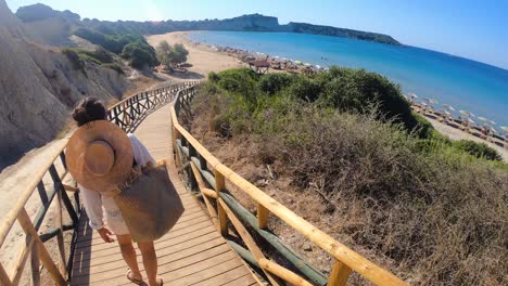 young woman walking towards zante beach on wooden walkway, zakynthos island, greece.