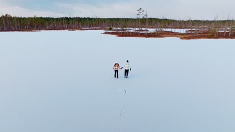Romantic couple skating hand in hand across Cenu bog lake in slow motion Latvia