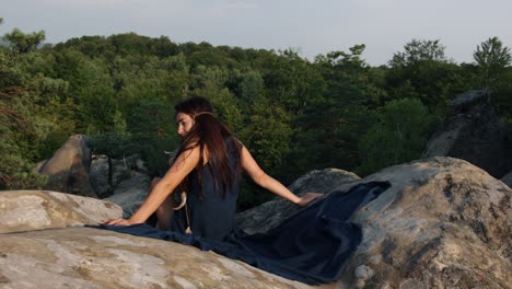 from behind, woman is seen in a dress flying gown fluttering in wind against background of rocks