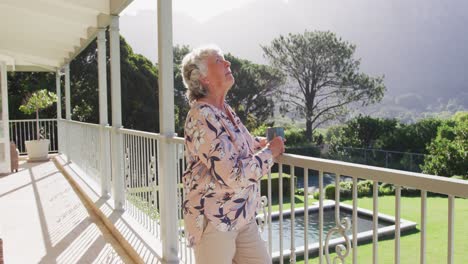 Smiling-caucasian-senior-woman-drinking-coffee-while-standing-in-the-balcony-at-home