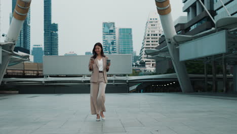 businesswoman walking in city, using phone and coffee