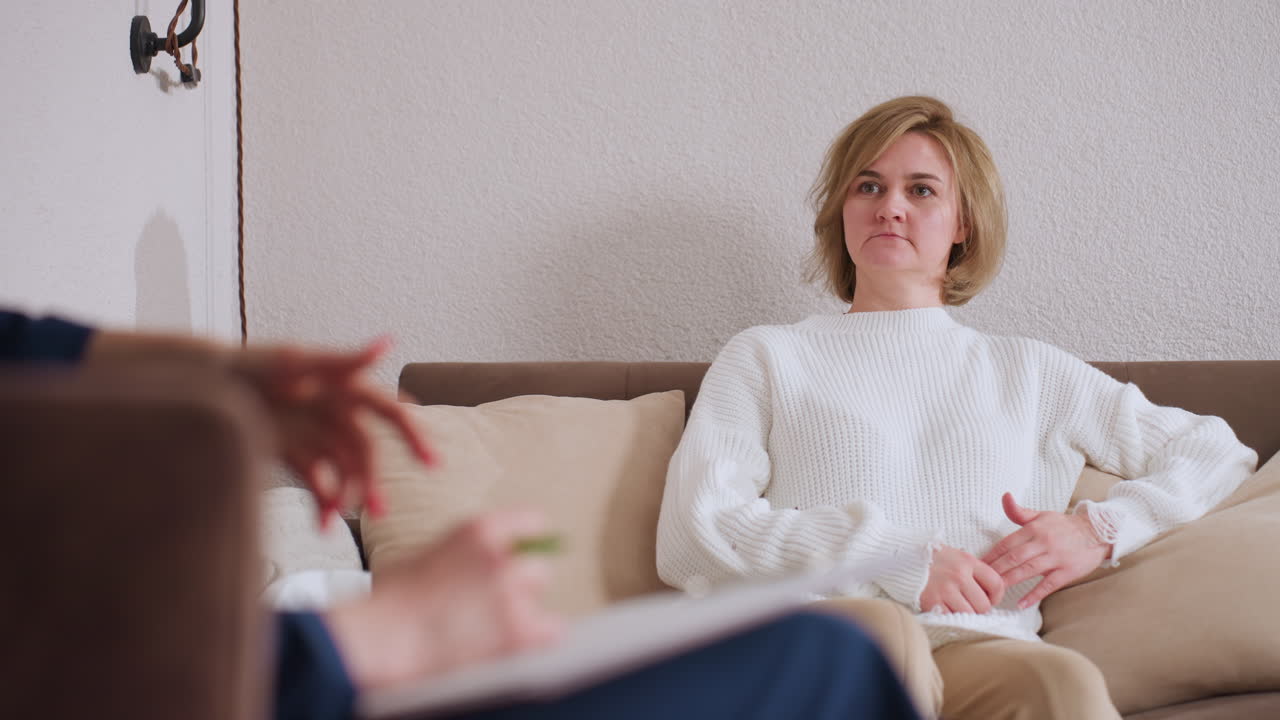 Individual seated during session expresses feelings with hand on chest, communicating emotionally in calm therapeutic environment, supportive conversation unfolds with focused attention