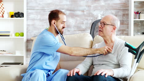 revealing shot of young male nurse listening to old retired man heartbeat