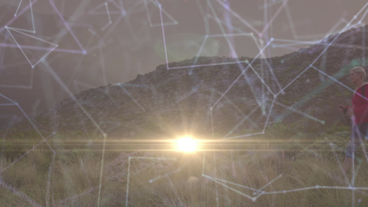 Female hiker using trekking pole on hillside with lens flare, showing technology network overlay