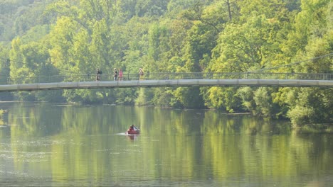 people walking across a suspensions bridge at the nahe river in bad kreuznach while another group is enjoying a boat ride