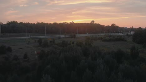 slow aerial flight over trees towards a highway outside nepean city, ontario at sunset with the sun shining over the hill and trees