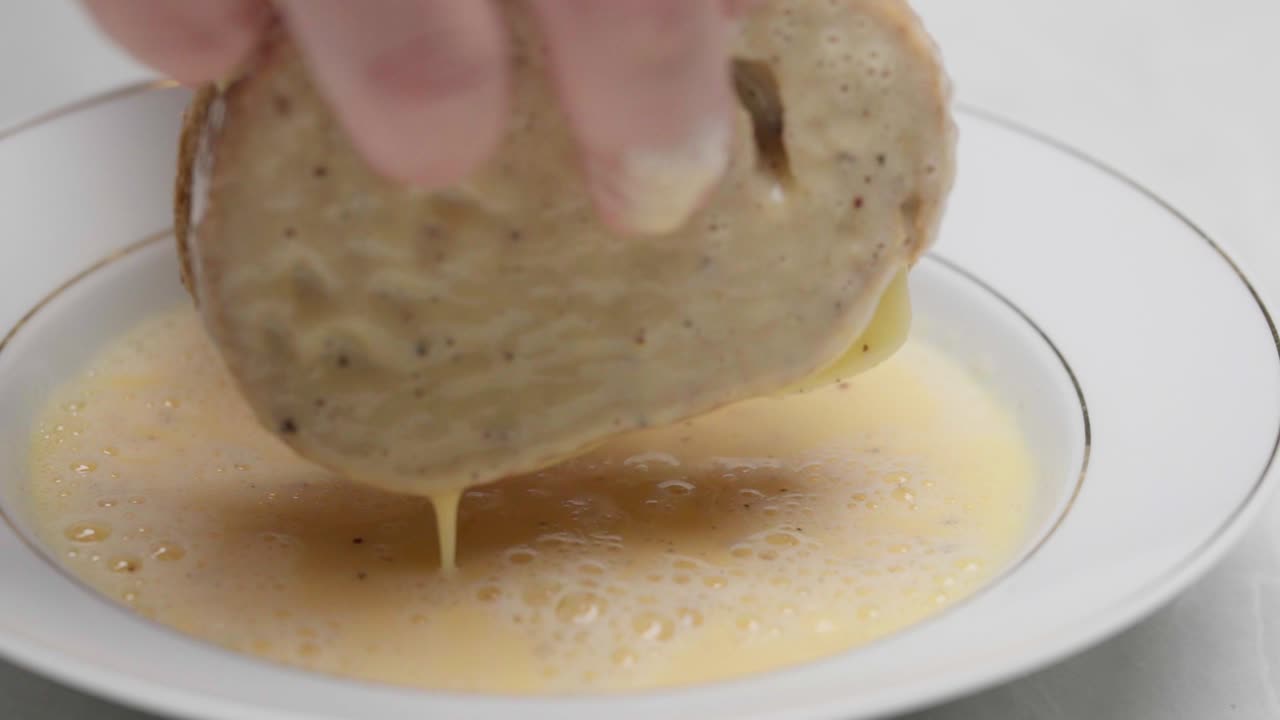 Primer plano de un sándwich mojándose en huevos batidos en un plato hondo, preparándose para la cocción
