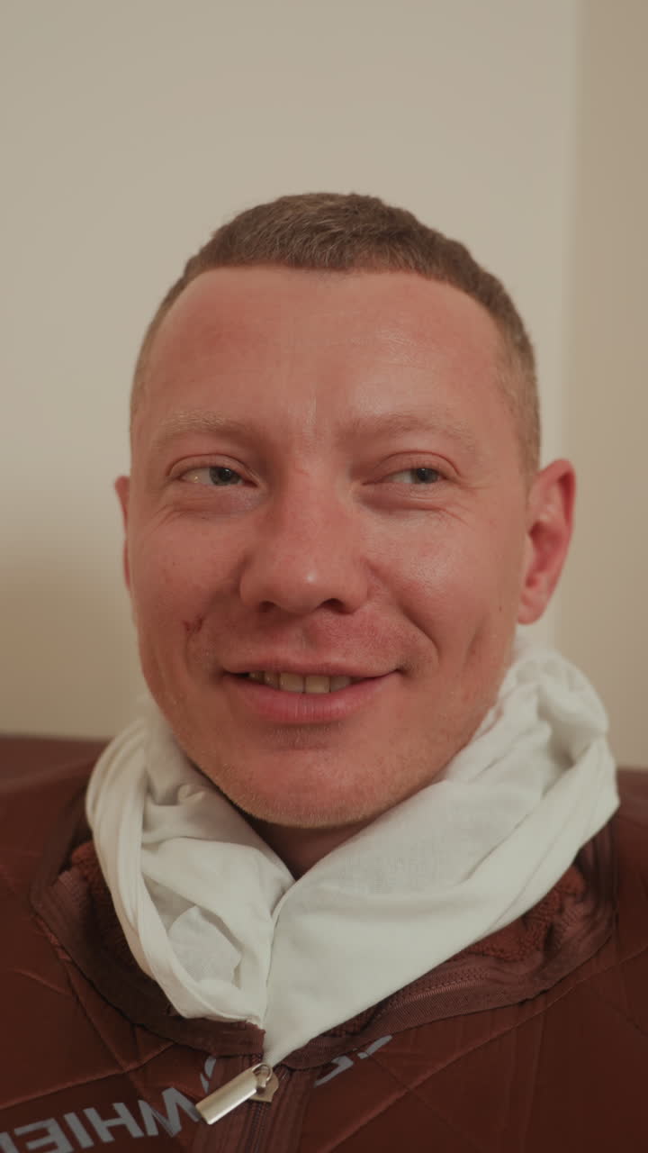 Uomo bianco in asciugamano dopo la terapia, primo piano di rilassamento facciale, cura post-trattamento in clinica estetica, asciugamano intorno al collo, sorriso sottile e pelle luminosa, luce ambientale calma, espressione soddisfatta