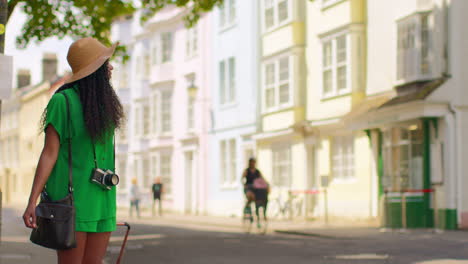 Turista-Femenina-Con-Cámara-De-Vacaciones-En-Oxford,-Reino-Unido,-Explorando-La-Ciudad-Caminando-Por-La-Calle-Holywell-Tirando-De-Una-Maleta-Con-Ruedas