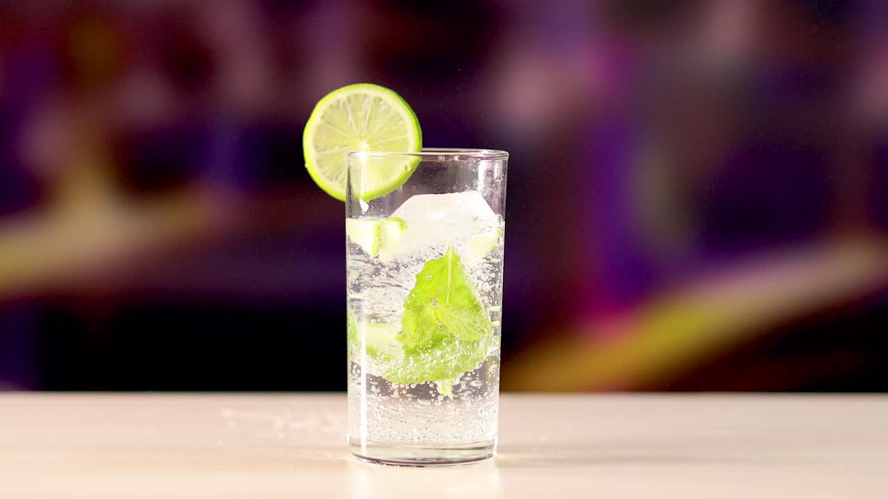 A vibrant mojito cocktail with lime and mint in a clear glass on a wooden surface, set against a colorful blurred background