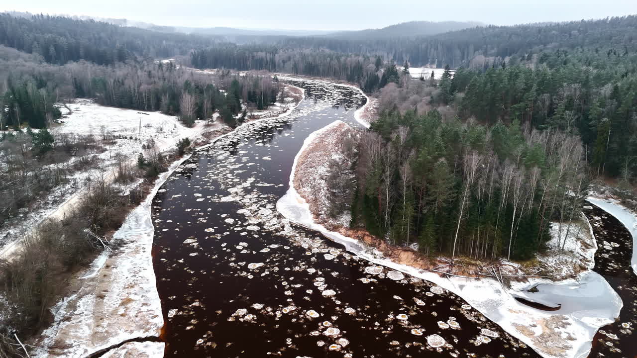 Ilmakuva jäisestä joesta, joka on täynnä kelluvia jäälohkareita ja mutkittelee metsän läpi