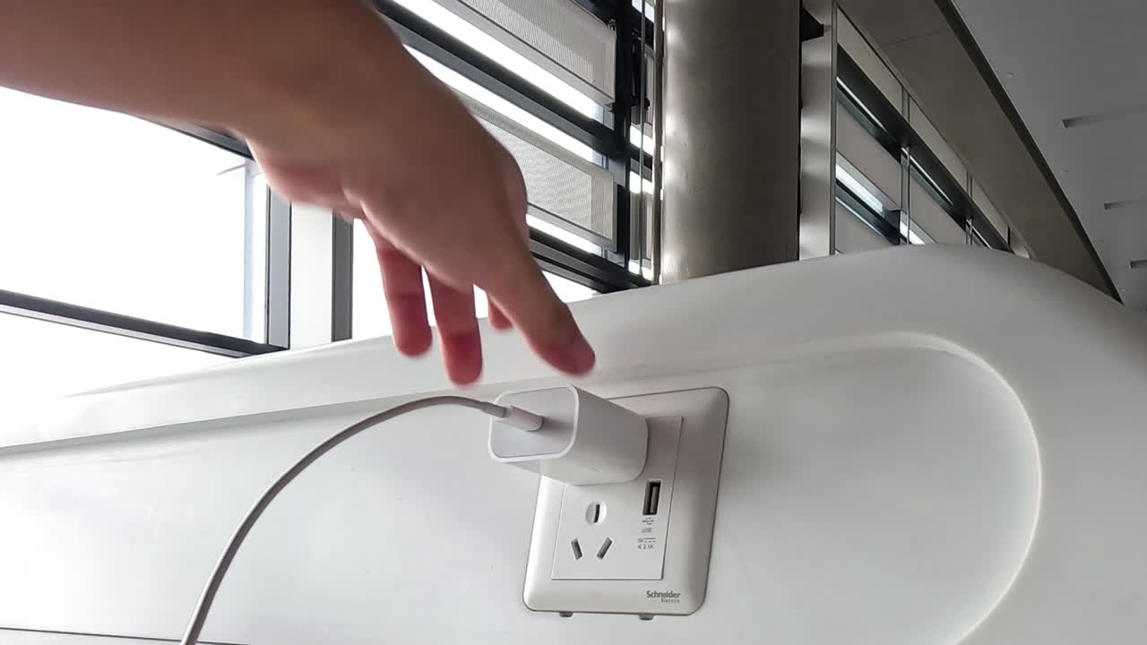 A person's hand inserts a white power adapter into a modern wall outlet indoors