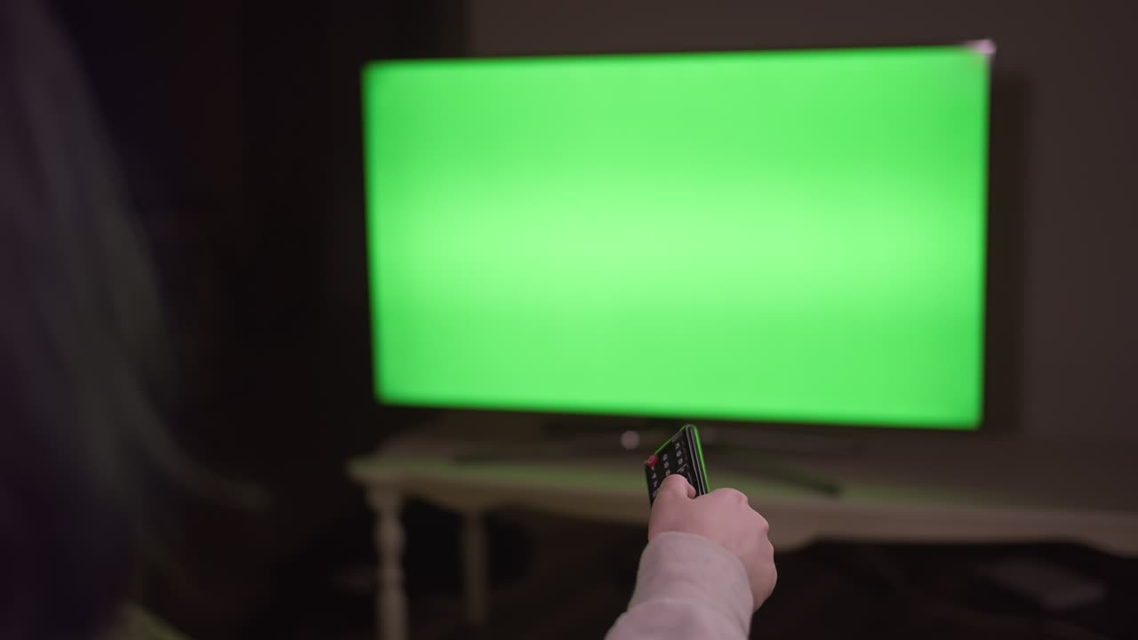 Una ragazza cambia canale premendo i pulsanti del telecomando, seduta di notte davanti alla TV