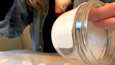 closeup of a woman painting a glass jar with white acrylic paint to use it as vase in an upcoming wedding