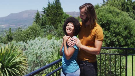 mixed race couple embracing each other and enjoying the view while standing in the balcony at home