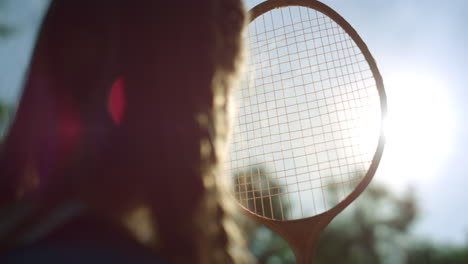 silhouette di una ragazza in primo piano che guarda il sole attraverso la rete della racchetta di badminton nel parco estivo.