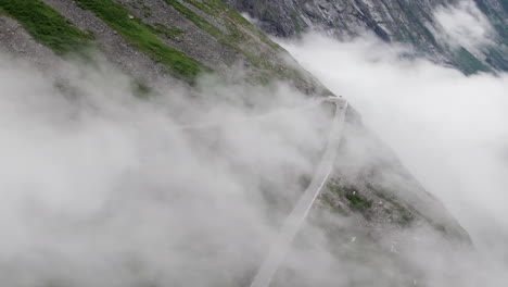 aerial shot circling around a cloud covered hairpin bend on the trollstigen in norway as it snakes down the steep valley side