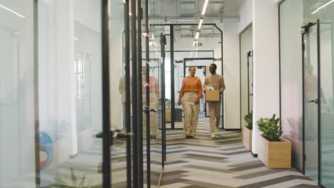 businesswoman accompanies a young man with a box along the corridor to his office