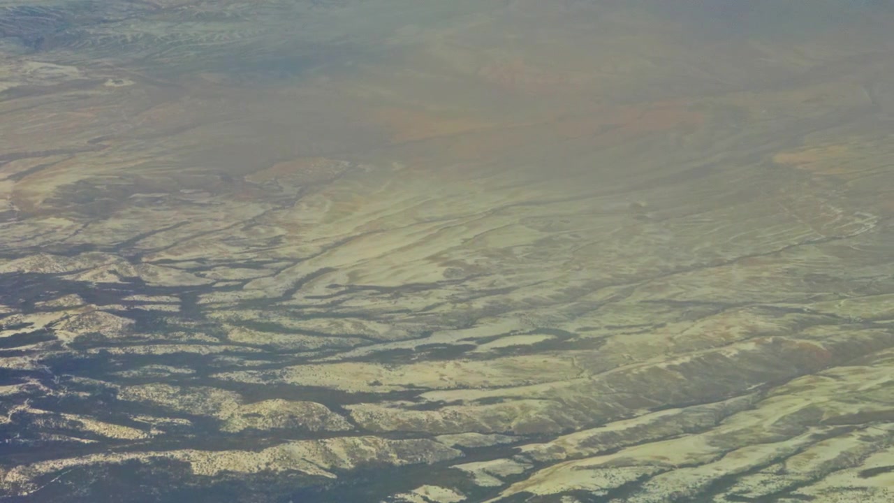 Layered ridgelines and sweeping erosion patterns across expansive landscape, aerial