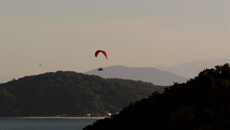 Distant silhouette of a paraglider soaring above the Atlantic Ocean between hills and mountains, Matinhos, Guaratuba, Paraná, Brazil