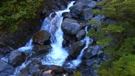 Waterfall-creek-passing-through-large-rocks-in-shade-of-early-morning-sunshine---Devil's-Punchbowl-Waterfall-Walk,-Arthur's-Pass-National-Park