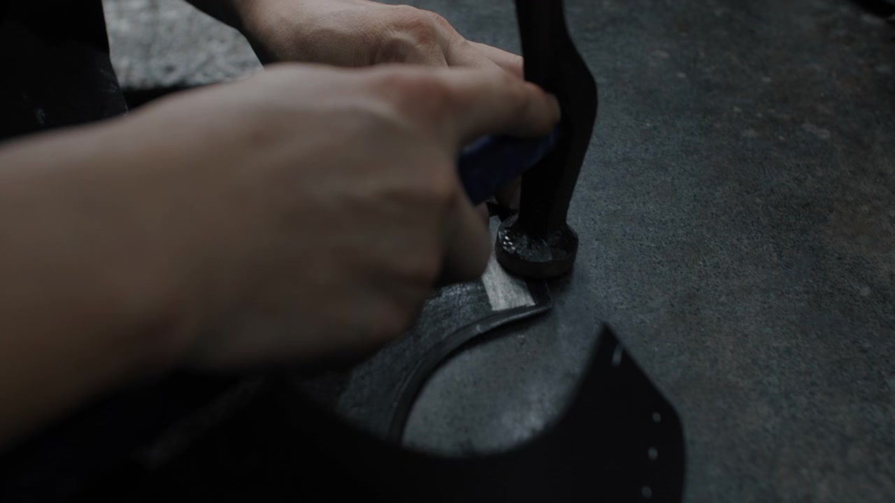 Hands cutting leather shoe parts on a workbench in a shoemaking workshop