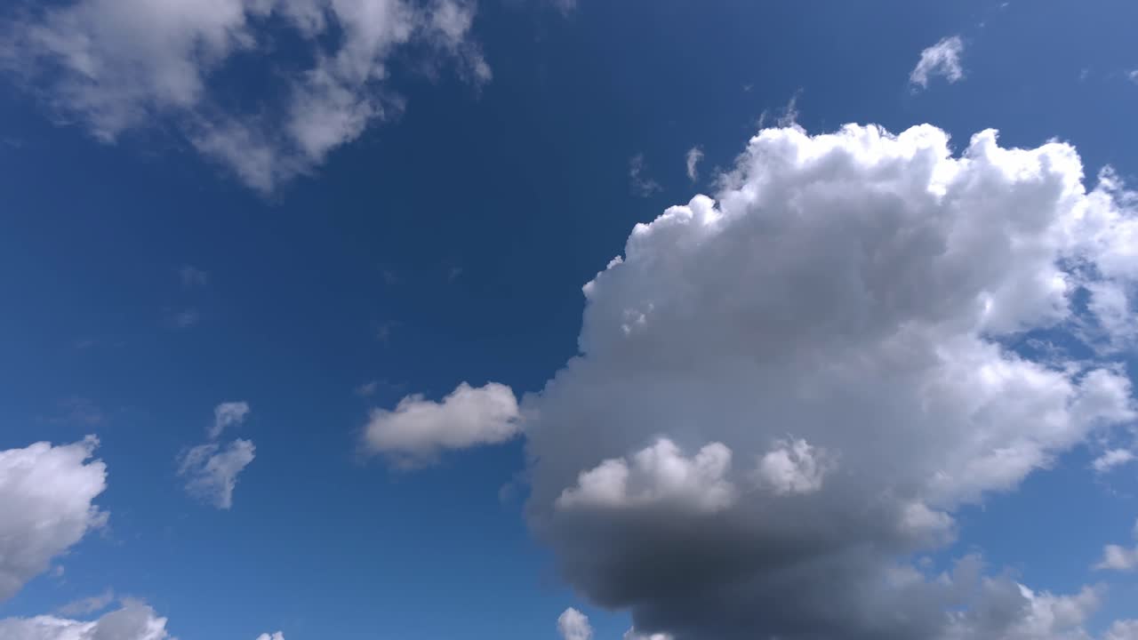 Wide timelapse showing cumulus clouds moving rapidly across bright blue sky on clear day. Atmospheric weather motion