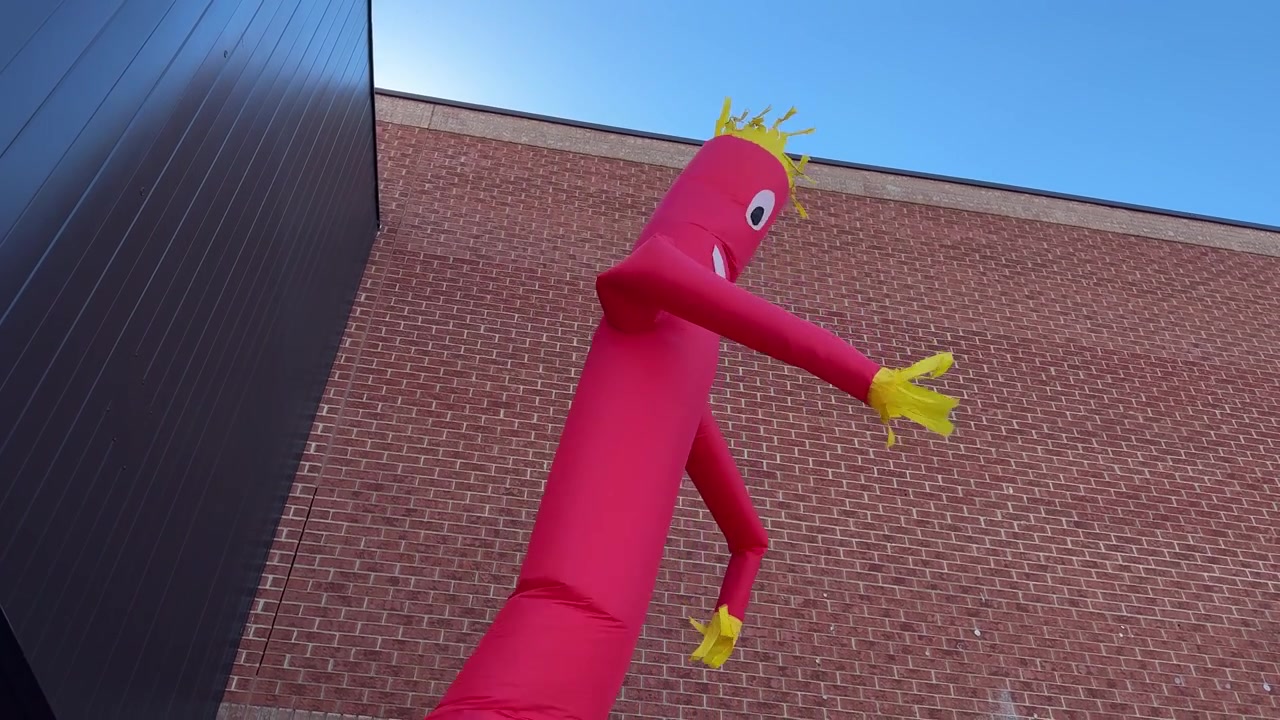 Red and yellow wacky waving tube man outdoors against brick wall and blue sky